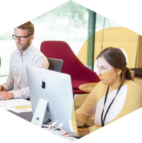 Image of two professionals working intently on their PCs in an office, with the aKUBE logo icon overlayed in the foreground.